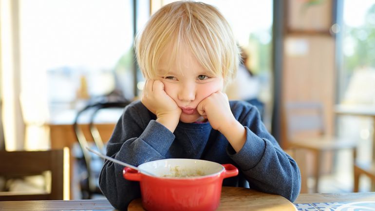 Et barn som sitter ved et bord med en bolle med mat